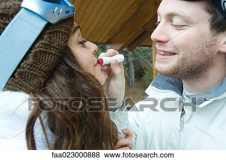 Stock Photo - Young man applying lipstick to girlfriend's lips, side view. Fotosearch