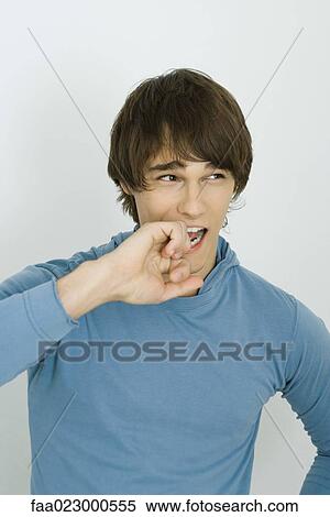 Stock Photography - Young man biting knuckles, looking away, portrait. Fotosearch