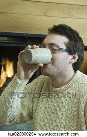 Young man drinking hot beverage by fireplace View Large Photo Image Picture - Young man drinking hot beverage by fireplace. Fotosearch