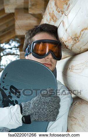 Young man holding snowboard, eyes closed, leaning against wall View Large Photo Image Stock Photograph - Young man holding snowboard, eyes closed, leaning against wall. Fotosearch