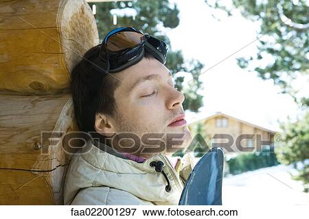 Young man leaning against log cabin, with snowboard, eyes closed View Large Photo Image Stock Photo - Young man leaning against log cabin, with snowboard, eyes closed. Fotosearch