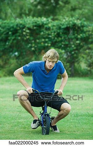 Young man riding small bicycle, full length View Large Photo Image Stock Photography - Young man riding small bicycle, full length. Fotosearch