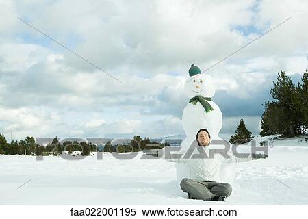 Young man sitting on ground in front of snowman, smiling, arms outstretched View Large Photo Image Stock Photography - Young man sitting on ground in front of snowman, smiling, arms outstretched. Fotosearch