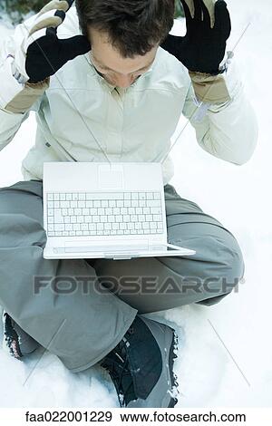 Young man sitting on the ground in snow, holding laptop computer on lap, hands raised View Large Photo Image Stock Photo - Young man sitting on the ground in snow, holding laptop computer on lap, hands raised. Fotosearch