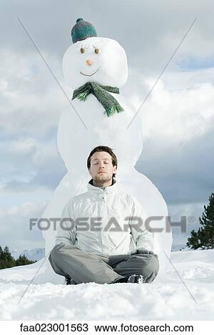 Young man sitting with legs crossed and eyes closed in front of snowman View Large Photo Image Stock Image - Young man sitting with legs crossed and eyes closed in front of snowman. Fotosearch