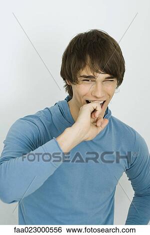 Stock Photograph - Young man smiling at camera, covering mouth with hand. Fotosearch