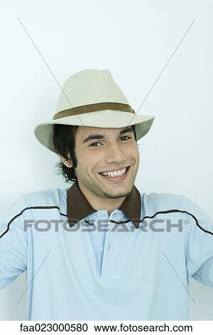 Young man smiling at camera, wearing hat, portrait View Large Photo Image Stock Image - Young man smiling at camera, wearing hat, portrait. Fotosearch