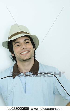 Young man smiling at camera, wearing hat, portrait View Large Photo Image Stock Photograph - Young man smiling at camera, wearing hat, portrait. Fotosearch