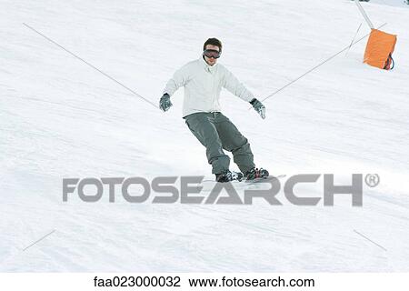 Young man snowboarding on ski slope, full length View Large Photo Image Stock Image - Young man snowboarding on ski slope, full length. Fotosearch