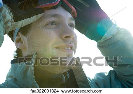 Picture - Young man taking off ski goggles, smiling. Fotosearch
