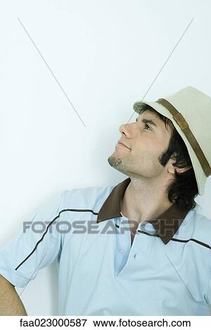Stock Photo - Young man wearing hat, looking up, portrait. Fotosearch