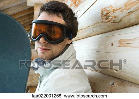 Young man with snowboard, looking at camera through ski goggles View Large Photo Image Stock Photography - Young man with snowboard, looking at camera through ski goggles. Fotosearch
