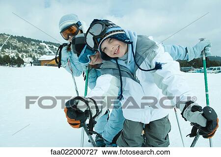 Young skiers on snow, leaning to side and smiling at camera, portrait View Large Photo Image Stock Photo - Young skiers on snow, leaning to side and smiling at camera, portrait. Fotosearch