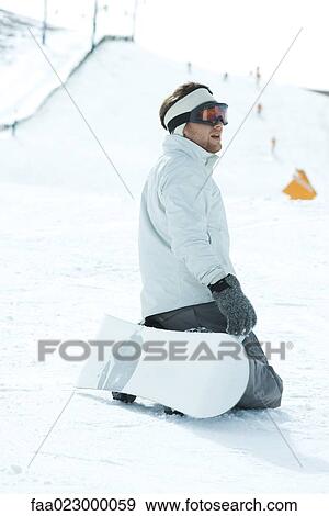 Young snowboarder kneeling on ski slope, looking away, side view View Large Photo Image Stock Photo - Young snowboarder kneeling on ski slope, looking away, side view. Fotosearch