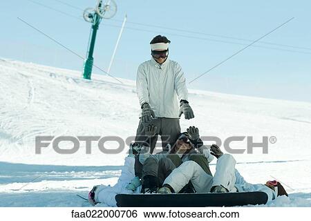Young snowboarders lying on ground reaching for young man standing behind them View Large Photo Image Stock Photograph - Young snowboarders lying on ground reaching for young man standing behind them. Fotosearch