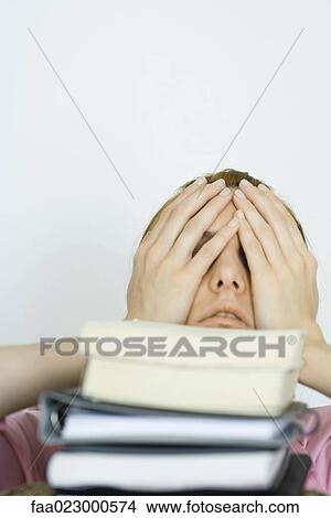 Young woman covering face with hands, stack of books in foreground View Large Photo Image Picture - Young woman covering face with hands, stack of books in foreground. Fotosearch