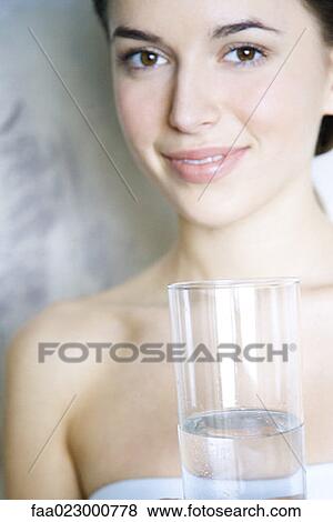 Stock Photo - Young woman holding glass of water, smiling at camera. Fotosearch