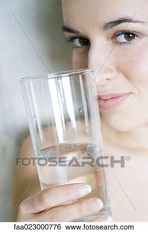 Young woman holding glass of water, smiling at camera, cropped view View Large Photo Image Stock Photograph - Young woman holding glass of water, smiling at camera, cropped view. Fotosearch