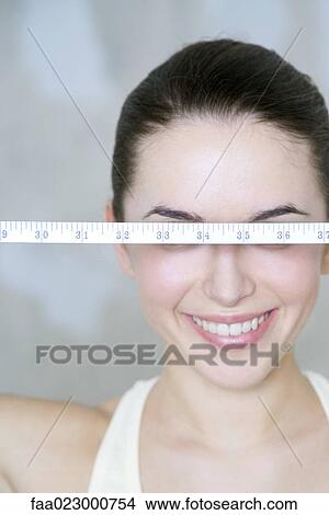 Young woman holding up measuring tape, eyes covered, smiling View Large Photo Image Picture - Young woman holding up measuring tape, eyes covered, smiling. Fotosearch