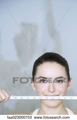 Young woman holding up tape measure, smiling at camera, portrait View Large Photo Image Stock Image - Young woman holding up tape measure, smiling at camera, portrait. Fotosearch
