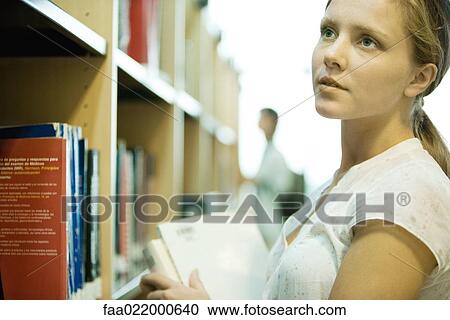 Young woman looking at shelves of books in library View Large Photo Image Stock Image - Young woman looking at shelves of books in library. Fotosearch