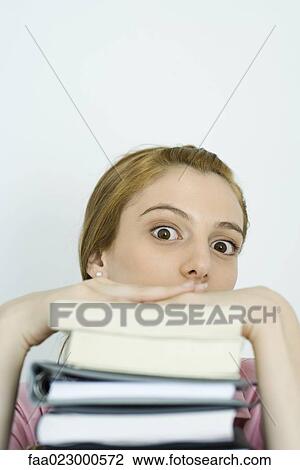 Young woman looking over stack of books at camera, wide eyes View Large Photo Image Stock Image - Young woman looking over stack of books at camera, wide eyes. Fotosearch