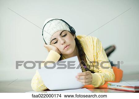 Young woman lying on floor listening to headphones and doing homework View Large Photo Image Picture - Young woman lying on floor listening to headphones and doing homework. Fotosearch