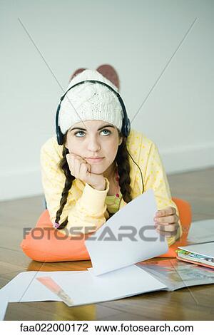 Young woman lying on floor listening to headphones and doing homework View Large Photo Image Stock Image - Young woman lying on floor listening to headphones and doing homework. Fotosearch