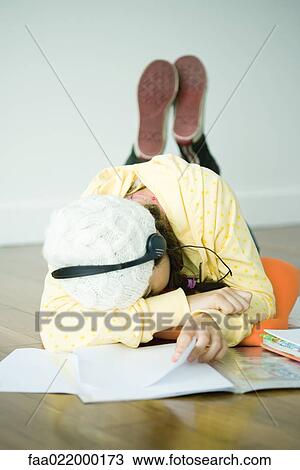 Stock Image - Young woman lying on floor listening to headphones, head on arm. Fotosearch