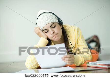 Stock Photography - Young woman lying on floor listening to headphones and doing homework. Fotosearch