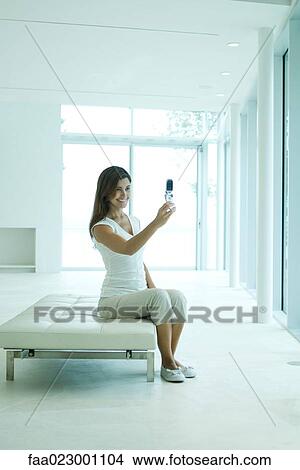 Young woman photographing self with cell phone, smiling, full length View Large Photo Image Picture - Young woman photographing self with cell phone, smiling, full length. Fotosearch