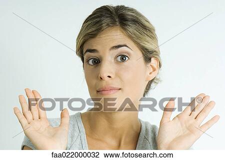 Stock Image - Young woman raising eyebrows, holding up palms, portrait. Fotosearch