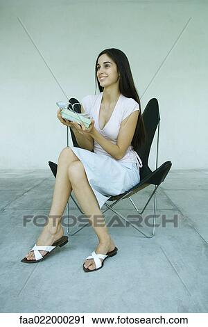 Young woman sitting in chair, holding up gift, full length portrait View Large Photo Image Stock Image - Young woman sitting in chair, holding up gift, full length portrait. Fotosearch