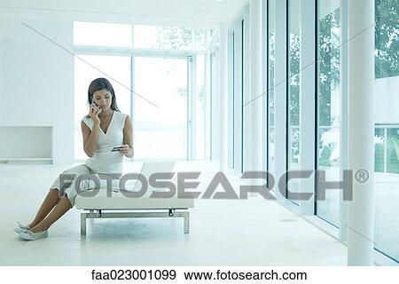 Stock Photo - Young woman sitting next to laptop computer, using cell phone, looking down at credit card. Fotosearch