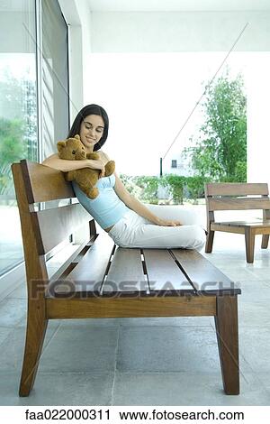 Young woman sitting on bench, holding teddy bear, full length portrait View Large Photo Image Stock Image - Young woman sitting on bench, holding teddy bear, full length portrait. Fotosearch