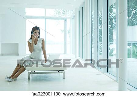 Young woman sitting on settee, using cell phone and laptop computer, smiling View Large Photo Image Stock Image - Young woman sitting on settee, using cell phone and laptop computer, smiling. Fotosearch