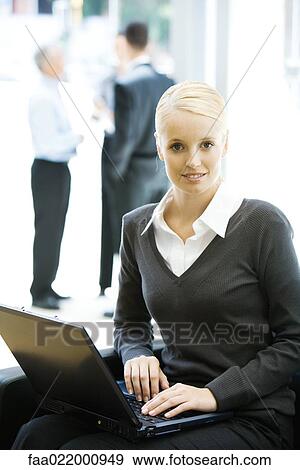 Young woman sitting, using laptop computer, smiling at camera View Large Photo Image Stock Photo - Young woman sitting, using laptop computer, smiling at camera. Fotosearch