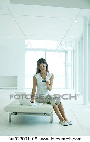 Young woman sitting, using laptop computer, looking down at credit card View Large Photo Image Stock Photography - Young woman sitting, using laptop computer, looking down at credit card. Fotosearch