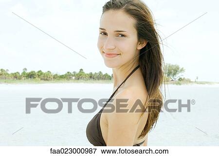 Stock Photo - Young woman smiling over shoulder at camera, wearing bikini, portrait. Fotosearch