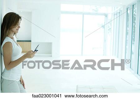 Young woman standing, looking at cell phone, side view View Large Photo Image Stock Image - Young woman standing, looking at cell phone, side view. Fotosearch