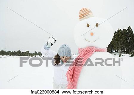 Young woman standing next to snowman, ready to throw snowball at camera View Large Photo Image Picture - Young woman standing next to snowman, ready to throw snowball at camera. Fotosearch