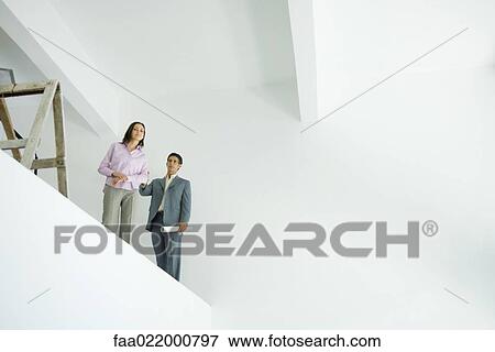 Stock Photo - Young woman standing with architect, looking over unfinished interior, low angle view. Fotosearch