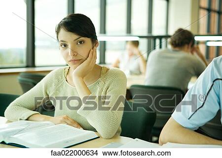 Picture - Young woman studying in university library, looking at camera. Fotosearch