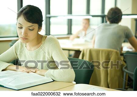 Stock Image - Young woman studying in university library. Fotosearch