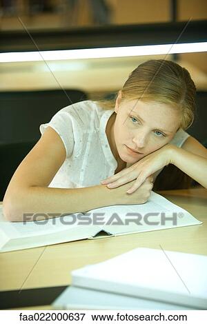 Young woman studying in university library, leaning on book and looking away View Large Photo Image Stock Photo - Young woman studying in university library, leaning on book and looking away. Fotosearch