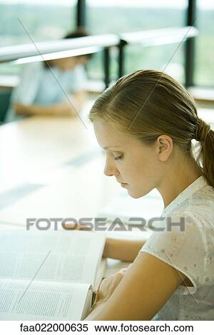 Stock Photography - Young woman studying in university library, side view. Fotosearch