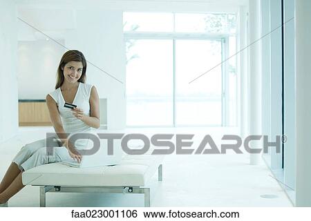 Stock Photograph - Young woman using laptop computer, holding credit card, smiling at camera. Fotosearch