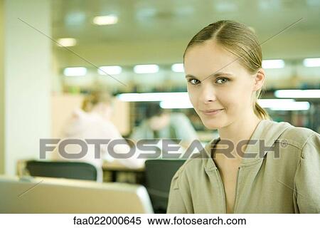 Young woman using laptop in library, smiling at camera View Large Photo Image Stock Photography - Young woman using laptop in library, smiling at camera. Fotosearch