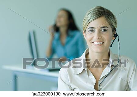 Young woman wearing headset in office, smiling at camera, portrait View Large Photo Image Stock Image - Young woman wearing headset in office, smiling at camera, portrait. Fotosearch