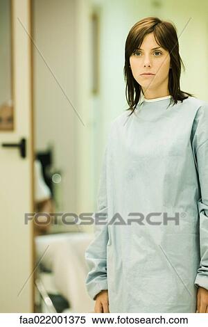 Stock Photography - Young woman wearing hospital gown, looking away, hospital corridor in background. Fotosearch
